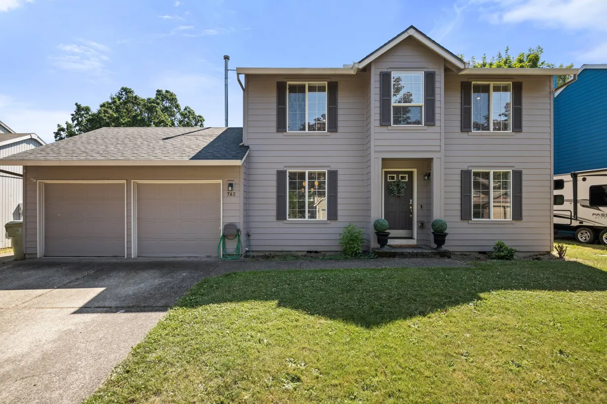 The image showcases a charming two-story single-family house in a quiet Hillsboro neighborhood. The home's double garage, spacious front porch, and well-kept lawn are prominently featured, suggesting ample space for families to gather, children to play, and guests to enjoy relaxing outdoor moments.