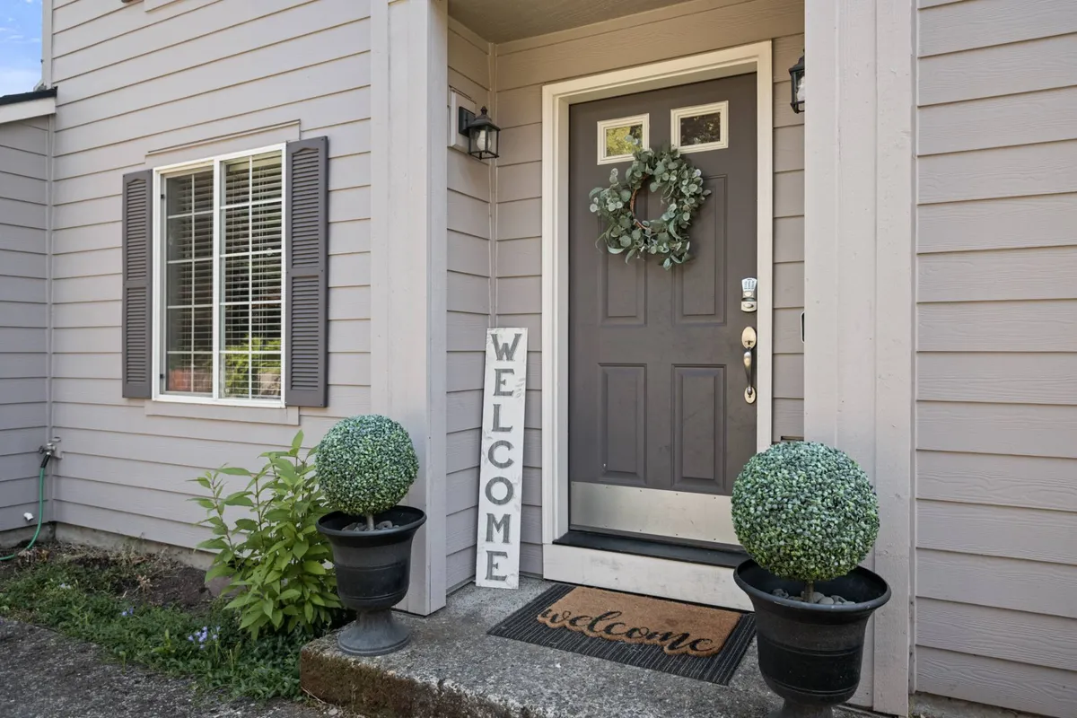 A welcoming front entrance of the home, featuring a friendly welcome sign, neat topiary plants, and a clean doormat. The scene is bright and inviting, offering a first glimpse of the property’s exterior and setting a pet-friendly tone for arrivals.