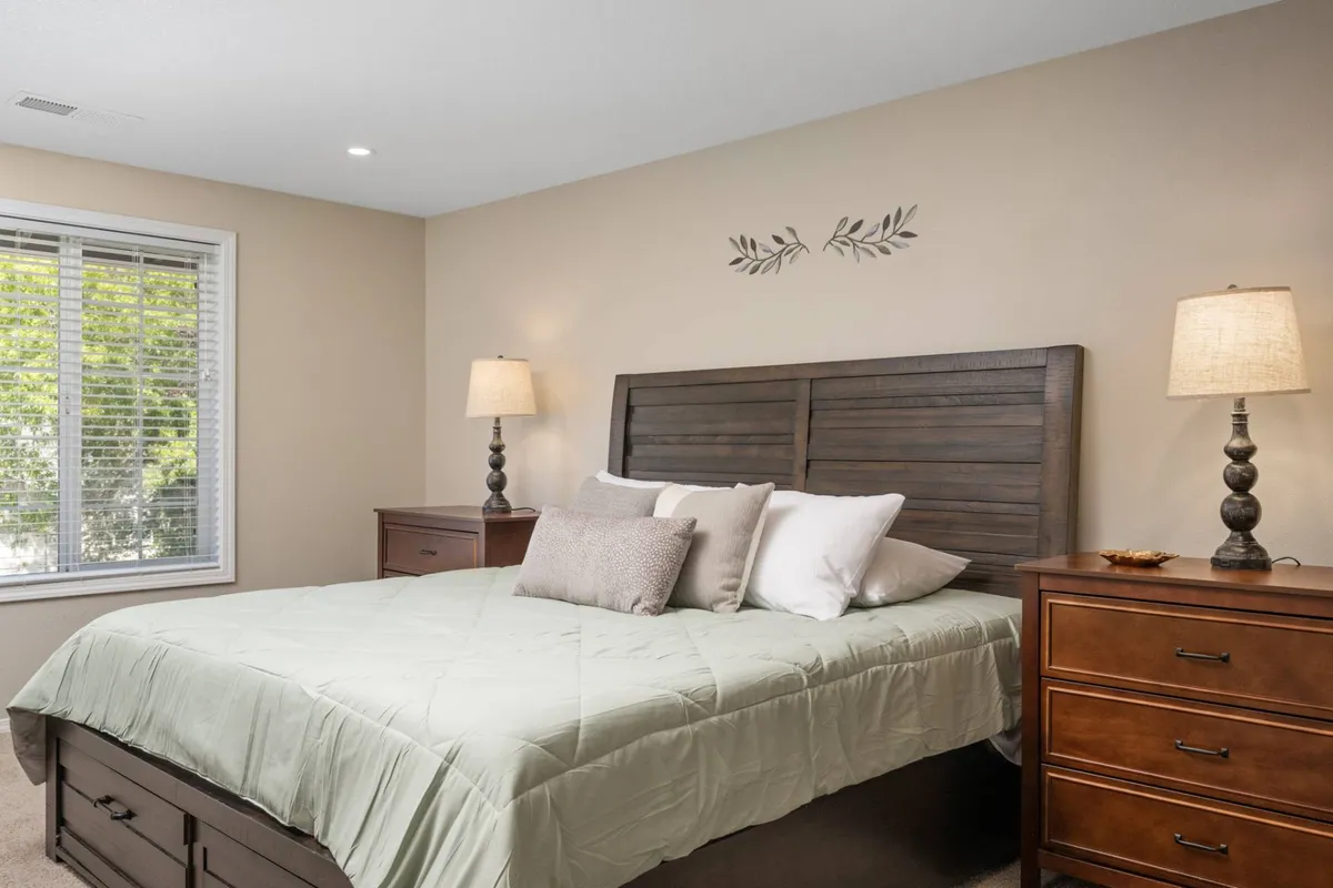 A serene bedroom with green bedding, a wooden headboard, and nightstands with lamps. The room is softly lit, evoking a sense of calm and comfort, ideal for restful nights and personal downtime.