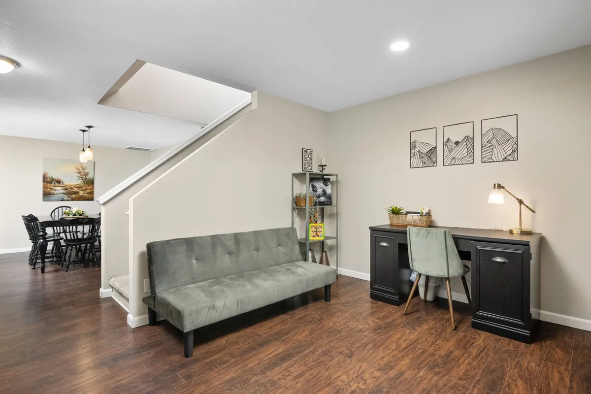 A secondary living space featuring a cozy sofa, a dedicated work desk, contemporary artwork, and a staircase leading to other areas. The room is designed for versatility—ideal for remote work, reading, or quiet relaxation.